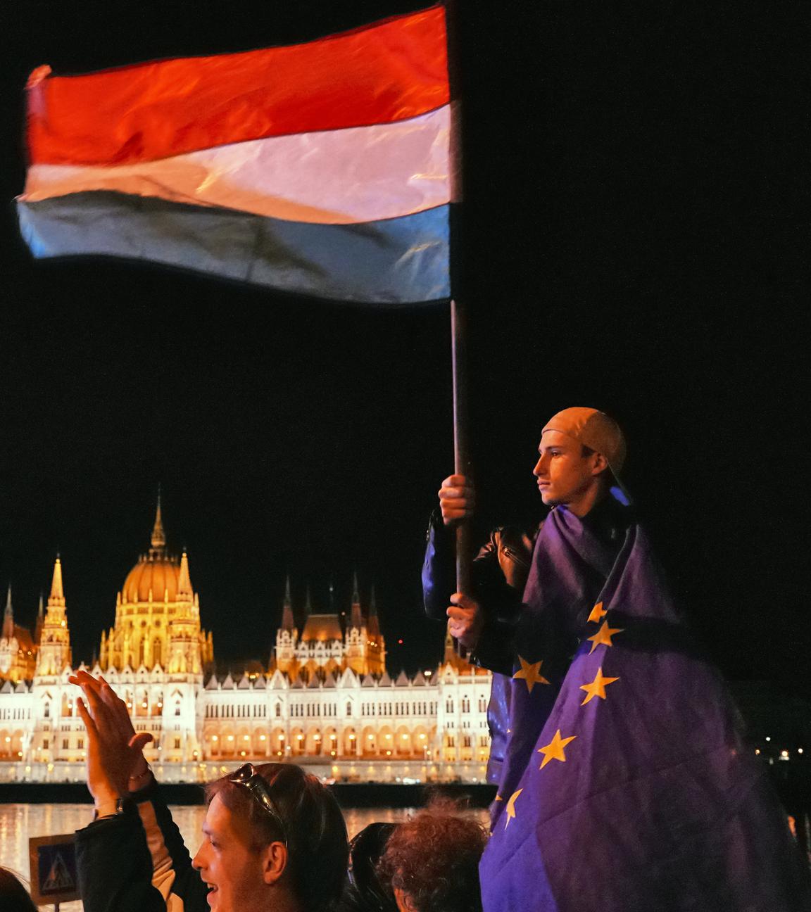 Ungarn: Budapest: Ein Mann ist in die Flagge der EU gehüllt und schwenkt die ungarische Flagge vor dem Parlamentsgebäude.