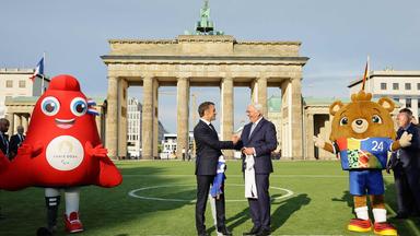 French President Emmanuel Macron and German President Frank-Walter Steinmeier shake hands as they exchance football shirts next to "Albaert" the official mascot of the UEFA Euro 2024 European Football Championship (R) and "Phryge" the Paris 2024 Olympic mascot, as they inaugurate the German-French Sports Summer 2024 in front of the Brandenburg Gate in Berlin, Germany on May 26, 2024. 