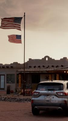 In Arizona ist ein Gebäude mit zwei gehissten USA-Flaggen zu sehen. Vor dem Auto steht ein Auto.