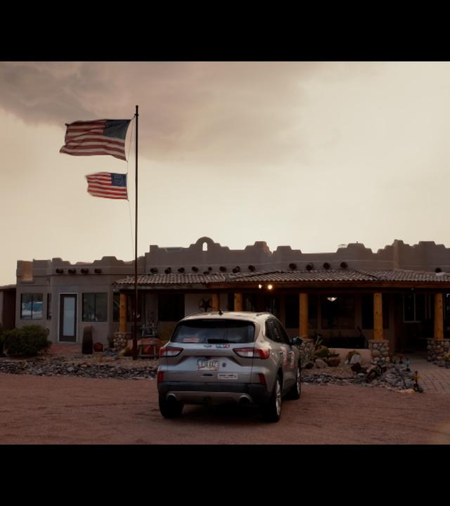 In Arizona ist ein Gebäude mit zwei gehissten USA-Flaggen zu sehen. Vor dem Auto steht ein Auto.