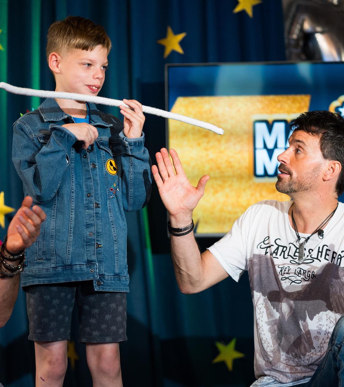 In einer Szene aus der ZDF-Doku "Magic Moves" stehen die Zauberer "Ehrlich Brothers" neben einem Kind, das gerade einen Zaubertrick vorführt.