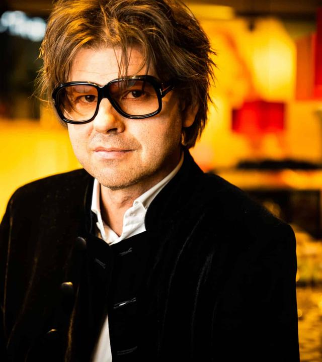 Magnus Lindgren, halbtotal mit "Straight-out-of-bed"-Frisur und einer übergroßen Brille, gelassen in die Kamera schauend.