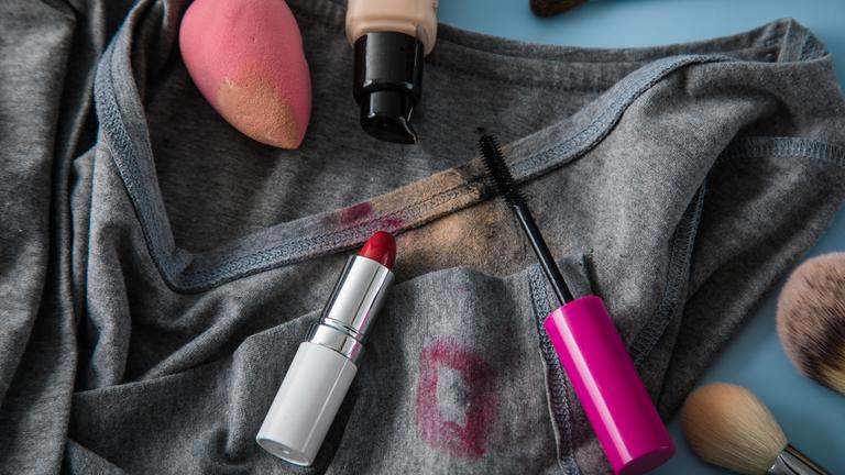 Ein T-Shirt mit Make-up-Flecken und verschiedenen Make-up-Utensilien.