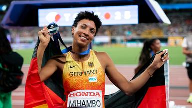 Malaika Mihambo hält eine Deutschlandfahne und eine Medaille.