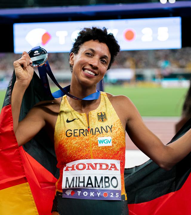 Malaika Mihambo hält eine Deutschlandfahne und eine Medaille.