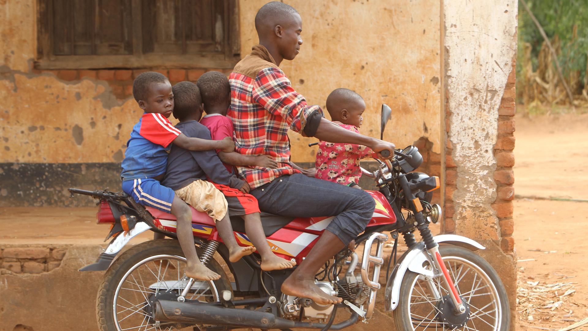 Ein Mann in Malawi transportiert vier Kinder auf einem Motorrad.