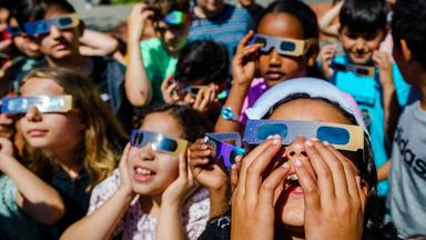 Einige Kinder stehen zusammen und haben Sonnenfinsternisbrille auf.