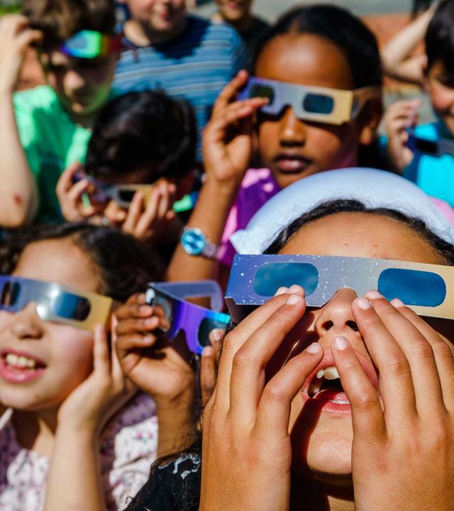 Einige Kinder stehen zusammen und haben Sonnenfinsternisbrille auf.