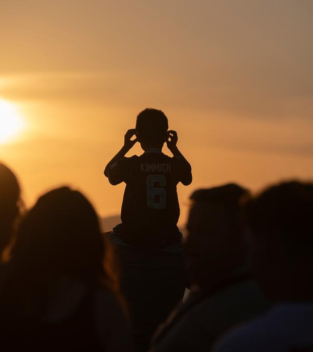 Ein Kind, das ein Fußballtrikot mit dem Namen des deutschen Fußballprofis Kimmich trägt, wartet mit weiteren Menschen am Strand von Palma auf die totale Sonnenfinsternis.