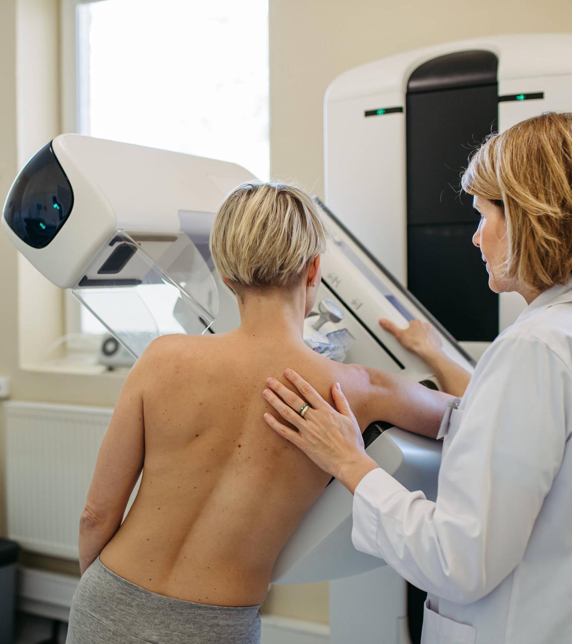 Eine Gesundheitsfachkraft richtet die Patientin für eine Mammographie ihrer Brust aus.