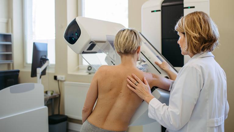 Eine Gesundheitsfachkraft richtet die Patientin für eine Mammographie ihrer Brust aus.