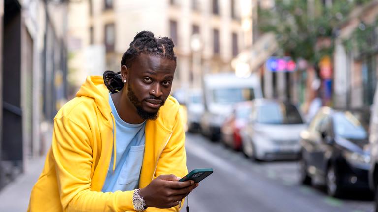 Junger Mann mit Afrohaaren lässt sich von Smartphone durch Stadt navigieren