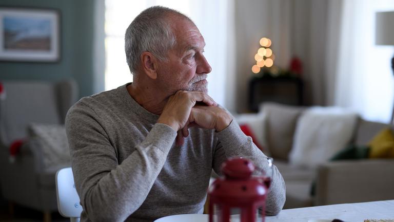 Älterer Mann sitzt alleine am Esstisch