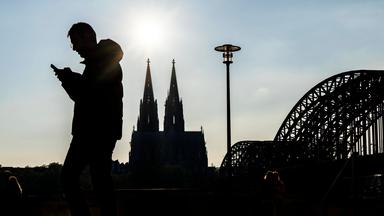 Silhouetten von einem Mann mit Handy in der Hand an der Rheinuferpromenade in Köln.