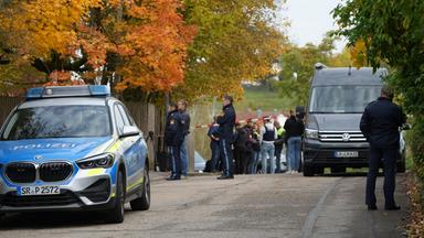 Einsatzkräfte der Polizei stehen nach einem Schusswechsel im Landkreis Dingolfing-Landau vor einem Wohngebäude auf der Straße.