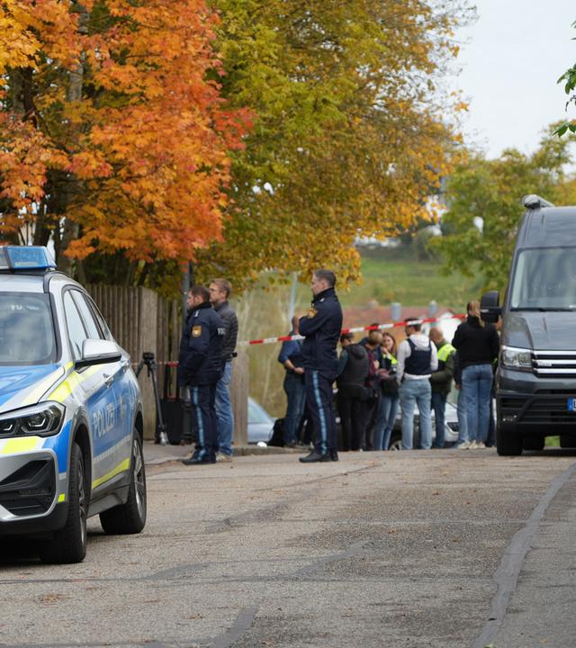 Einsatzkräfte der Polizei stehen nach einem Schusswechsel im Landkreis Dingolfing-Landau vor einem Wohngebäude auf der Straße.