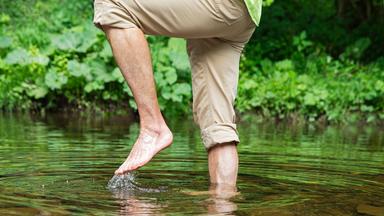 Ein Mann läuft barfuß druch einen Fluss.