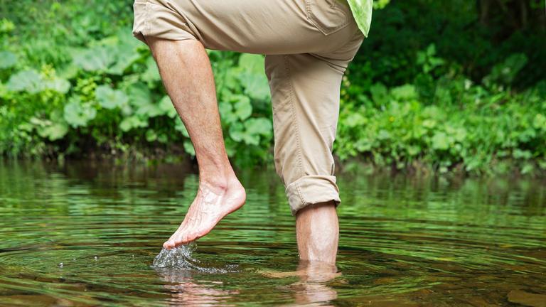 Ein Mann läuft barfuß druch einen Fluss.