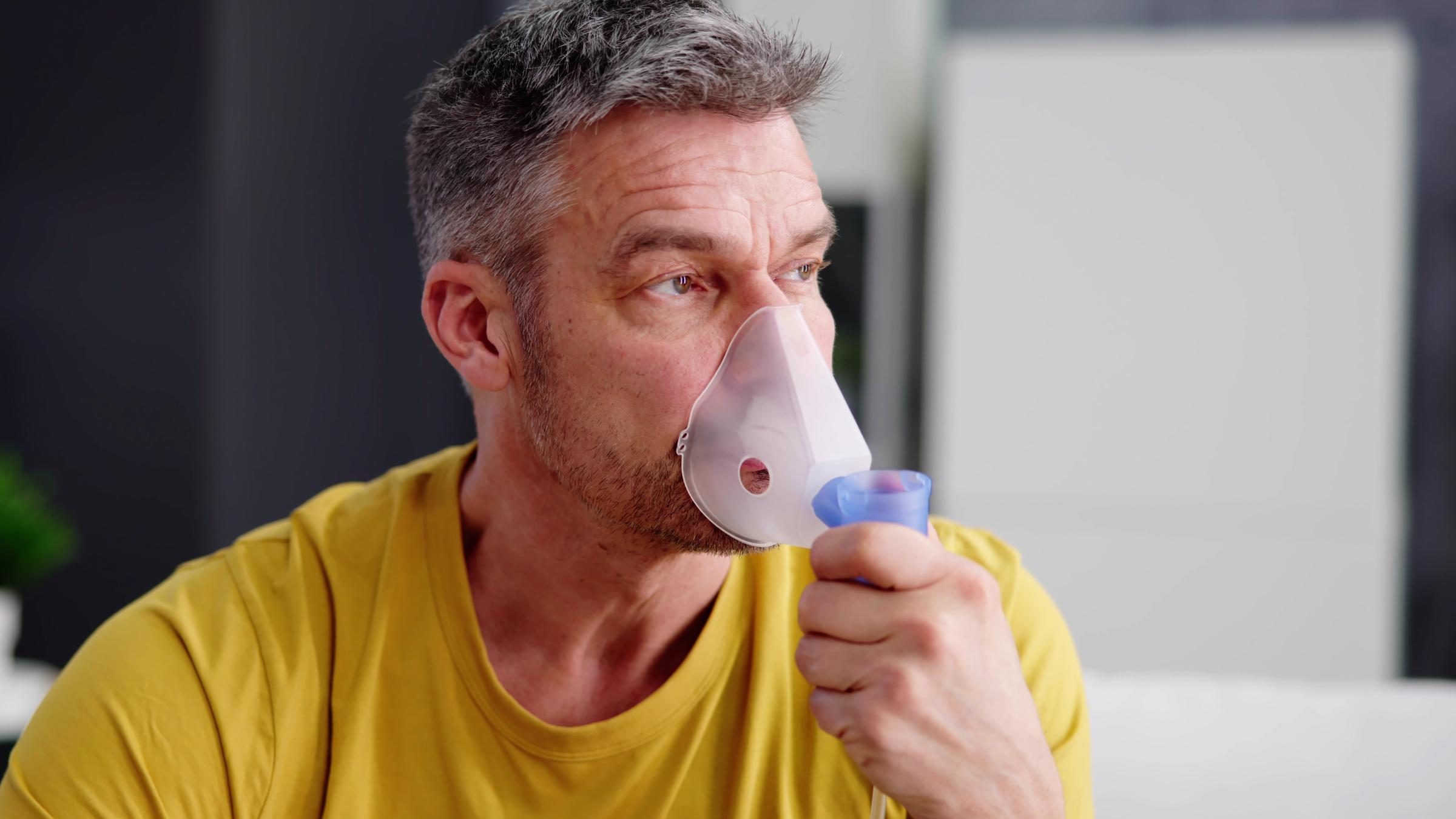 Ein Mann inhaliert über eine Maske auf der Nase.