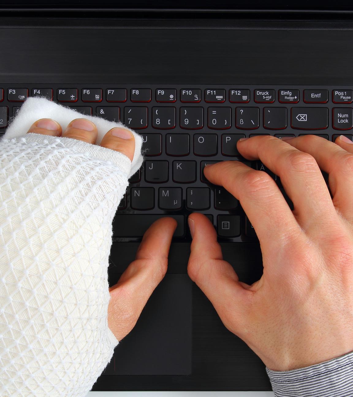 Mann mit Gipsarm bedient Tastatur