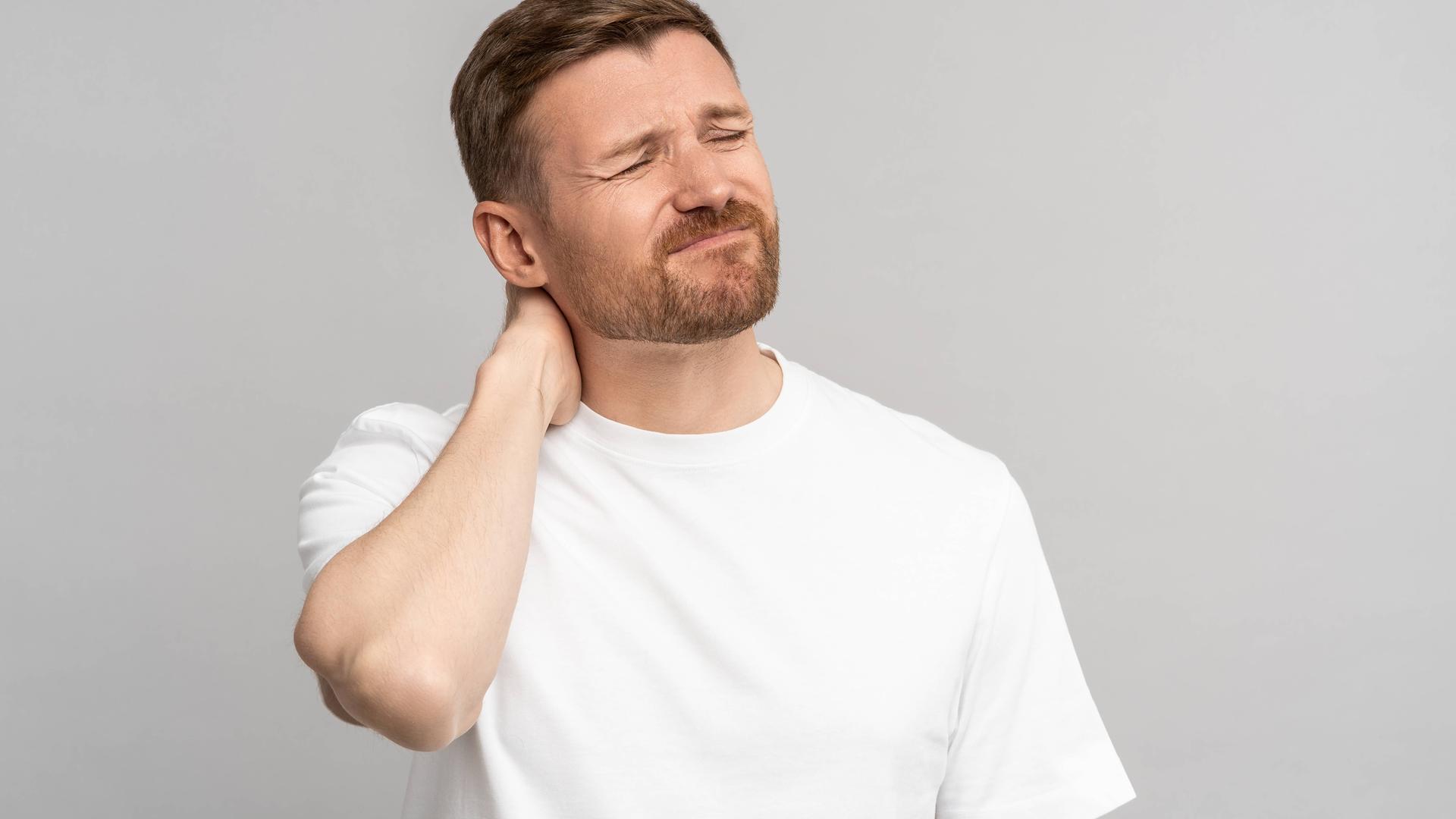 Ein Mann hält sich mit schmerzverzehrtem Gesicht den Nacken und die Schulter.