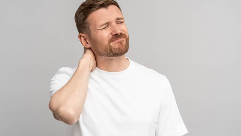 Ein Mann hält sich mit schmerzverzehrtem Gesicht den Nacken und die Schulter.