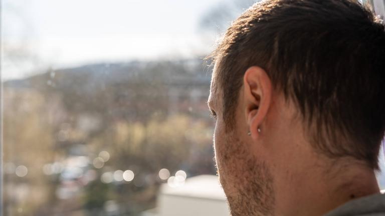Ein junger Mann schaut nachdenklich aus dem Fenster. Er scheint sehr niedergeschlagen und einsam.