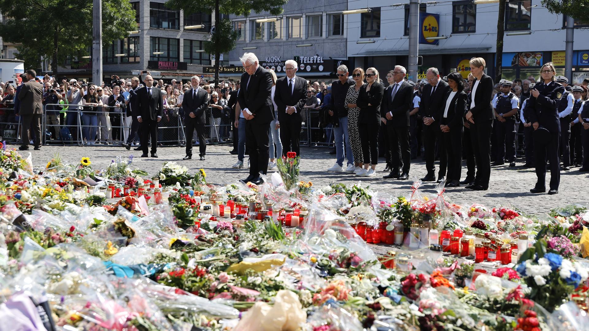 Bundespräsident Frank-Walter Steinmeier und der baden-württembergische Ministerpräsident Winfried Kretschmann stehen für eine Schweigeminute mit den Angehörigen des getöteten Polizisten am Tatort nach dem Messerangriff letzte Woche in der Mannheimer Innenstadt