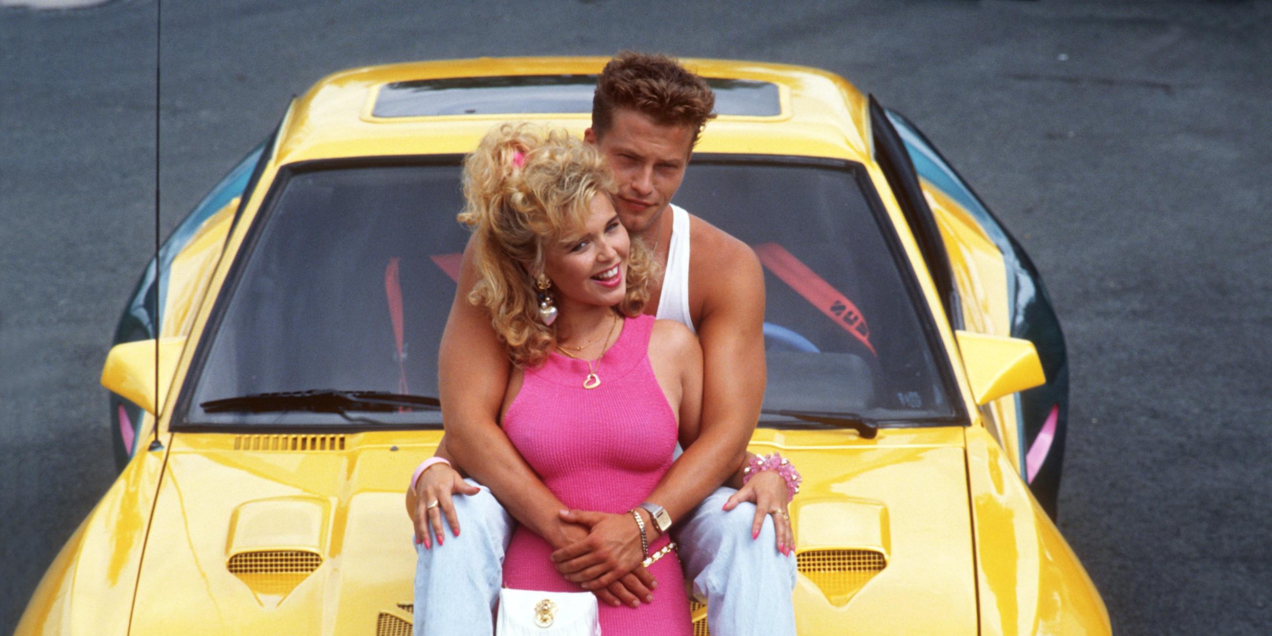 Auf der Motorhaube eines Opel Manta sitzen zwei Menschen, die Schauspieler Tina Ruland und Til Schweiger.