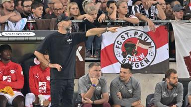 FC St. Pauli - RB Leipzig am 22.09.2024: RB-Trainer Marco Rose deutet Richtung Spielfeld. Im Hintergrund St.-Pauli-Fans auf der Tribüne.