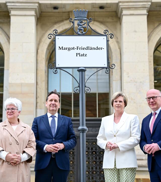 07.05.2026, Berlin: Stefanie Remlinger (Bündnis 90/Die Grünen, l-r), Bezirksbürgermeisterin Berlin Mitte, Karsten Dreinhöfer, Vorsitzender des Vorstandes der Margot Friedländer Stiftung, Cornelia Seibeld (CDU), Präsidentin des Abgeordnetenhauses, und Kai Wegner (CDU), Regierender Bürgermeister von Berlin, stehen während einer Feierstunde zur Umbenennung des Platzes unter dem Schild Margot-Friedländer-Platz vor dem Berliner Abgeordnetenhaus.