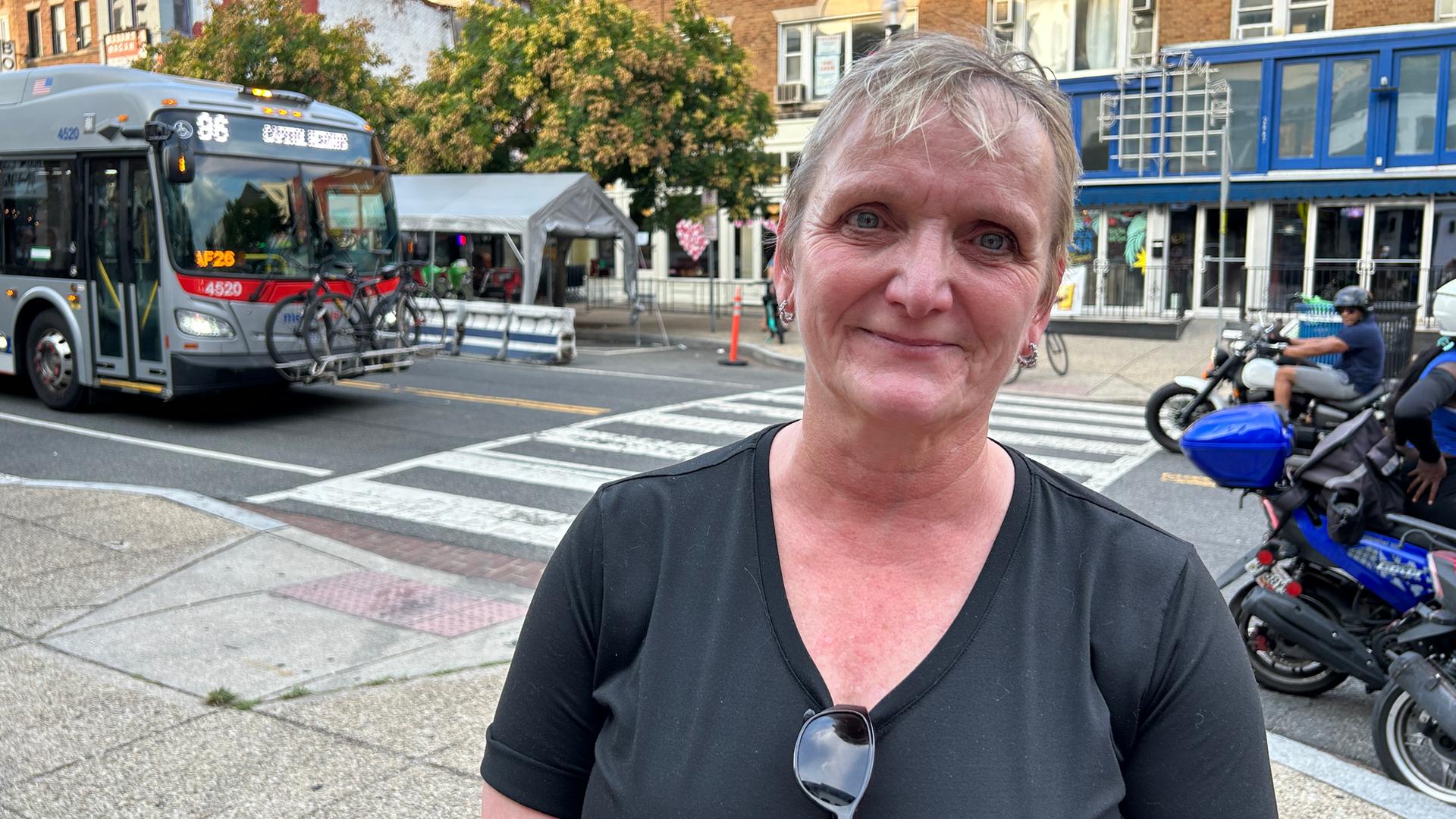 Eine ältere Dame mit Kurzharrschnitt seht am Rande einer Straße.