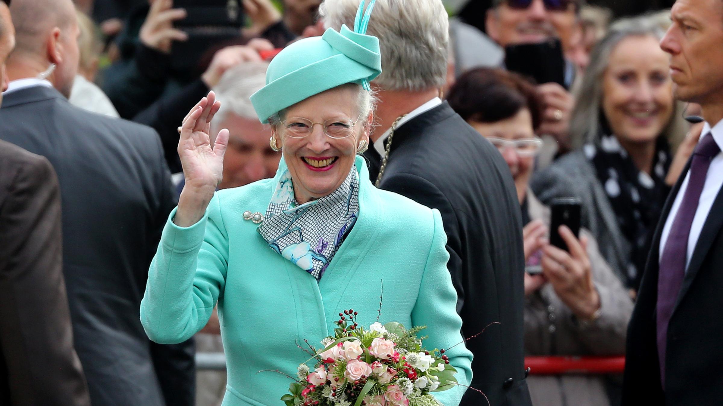 Das Bild zeigt Königin Margrethe II. von Dänemark, wie sie winkend durch eine Menschenmenge schreitet.
