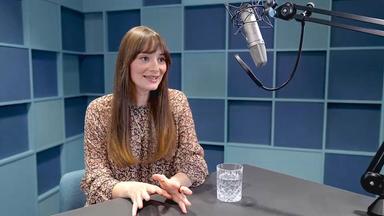Maria Ehrich sitzt in einem Tonstudio an einem Tisch vor einem Studiomikrofon. Auf dem Tisch steht ein Glas Wasser.