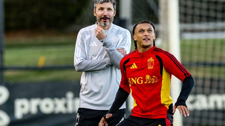 Belgischer Trainer steht lächelnd hinter Spieler und beide schauen auf den Ball.