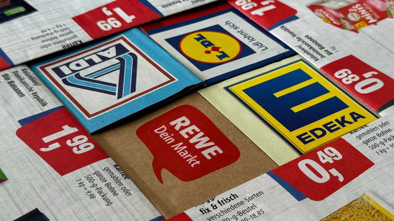 Logos und Prospekte von Edeka, Rewe, Aldi und Lidl liegen eng beisammen.