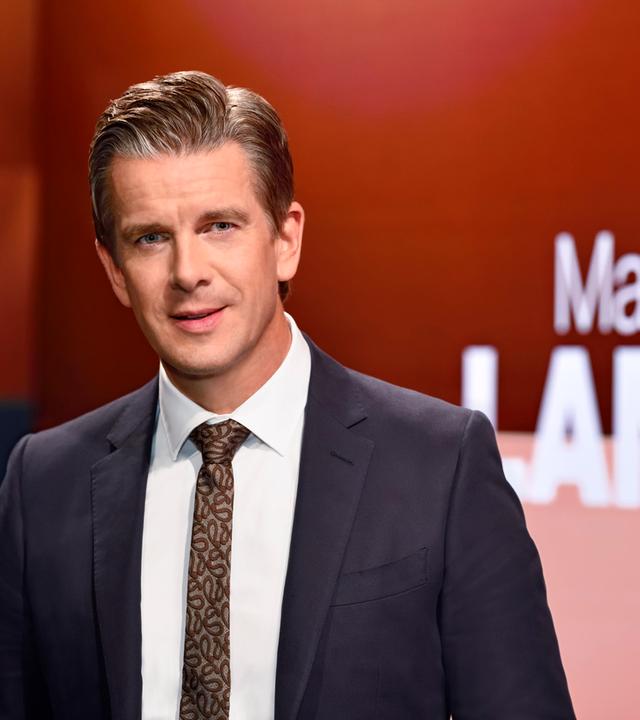 Markus Lanz - Moderator. Zu sehen in Anzug und gut friesiert. Neben Ihm sein Name als Schriftzug