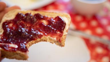 06.03.2023, Hessen, Gießen: Ein Mann hält ein Toastbrot mit Himbeermarmelade in der Hand.