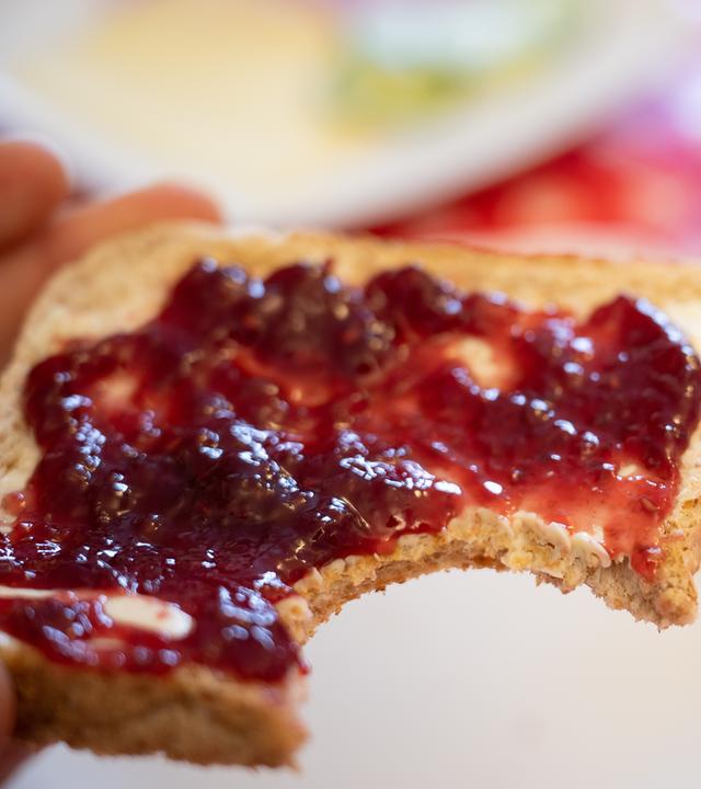 06.03.2023, Hessen, Gießen: Ein Mann hält ein Toastbrot mit Himbeermarmelade in der Hand.