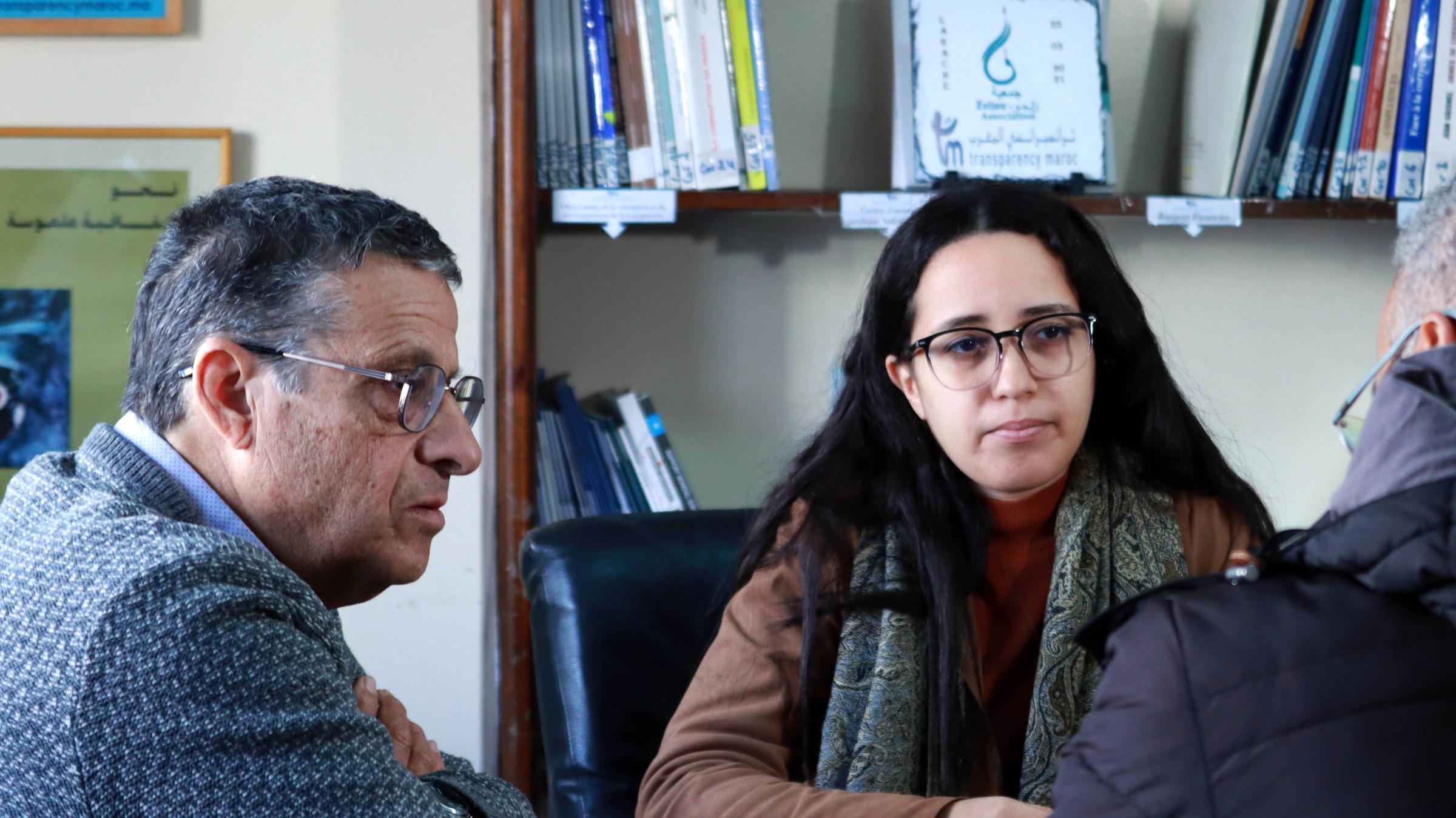 Zwei Männer und eine Frau sitzend im Gespräch vor Bücherregal.