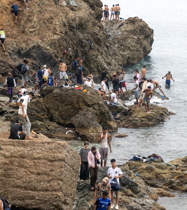 Menschen stehen an einem Ufer, während sie versuchen, von der nordmarokkanischen Stadt Fnideq in die spanische Exklave Ceuta zu gelangen.