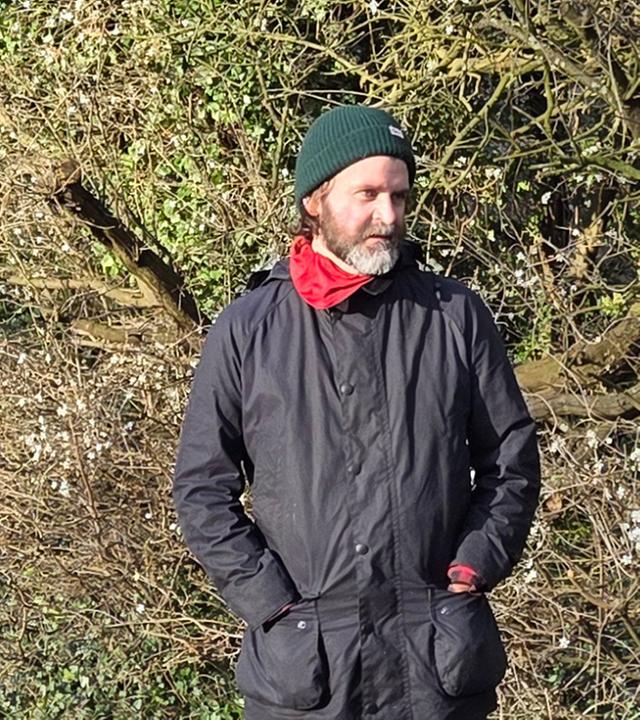 Mann steht vor Gebüsch