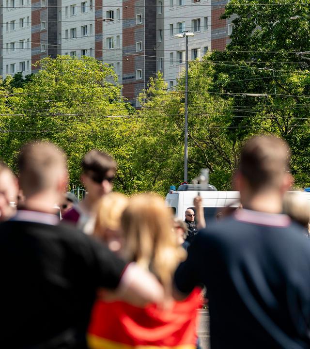 Eine Gruppe unscharf vvon hinten fotografierter Jugendlicher in schwarzen T-Shirts und mit Kurzhaarfrisuren. Ein Mädchen hat sich eine Deutschlandflagge umgebunden.