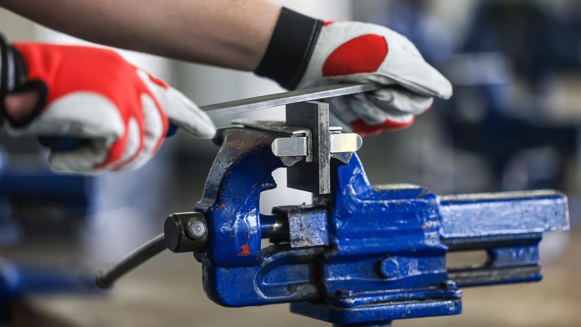 Ein Auszubildender zum Mechatroniker bearbeitet in einer Ausbildungswerkstatt an einem Schraubstock ein Werkstück