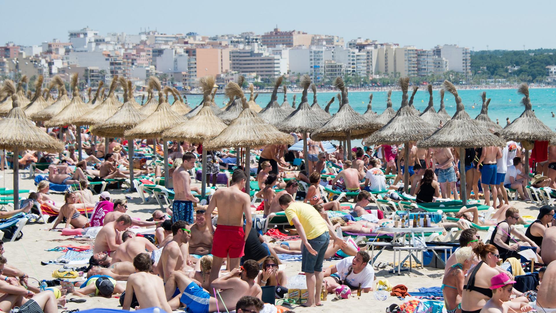 Menschen liegen dicht gedrängt am Strand, im Hintergrund Hochhäuser