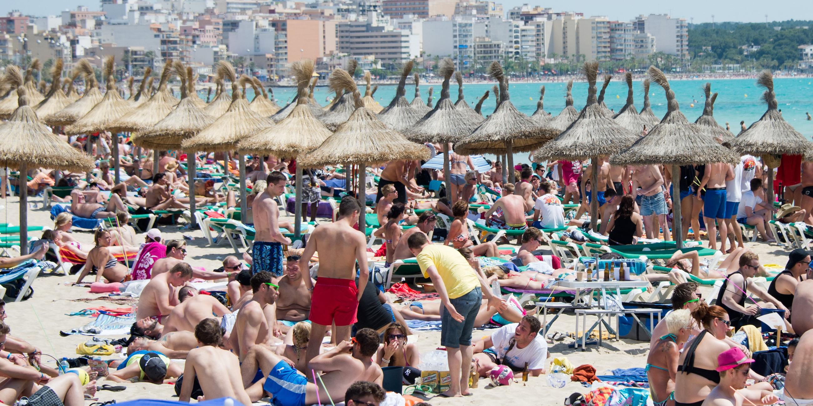 Menschen liegen dicht gedrängt am Strand, im Hintergrund Hochhäuser