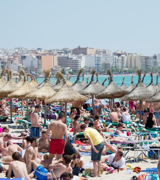 Menschen liegen dicht gedrängt am Strand, im Hintergrund Hochhäuser