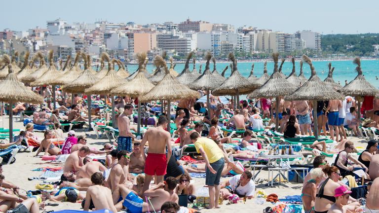 Menschen liegen dicht gedrängt am Strand, im Hintergrund Hochhäuser