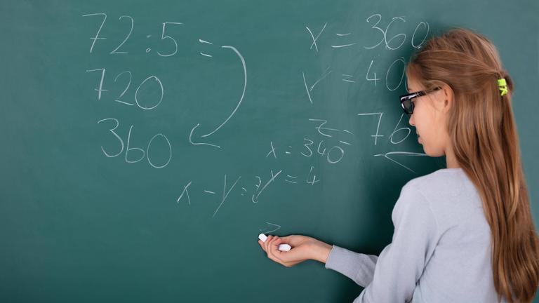 Schülerin steht an einer Tafel und rechnet.