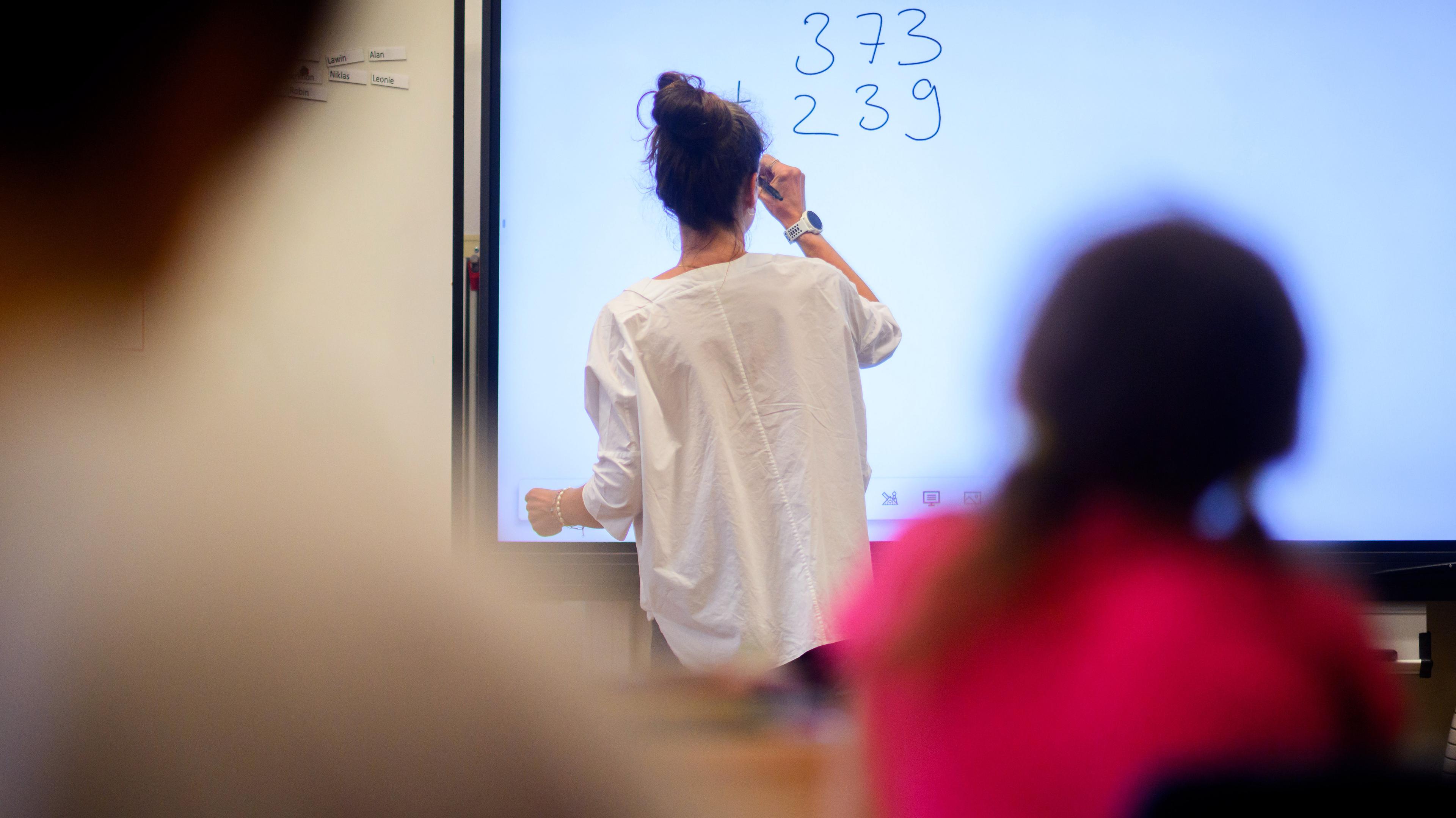 Eine Lehrerin schreibt eine Mathematikaufgabe auf eine digitale Schultafel im Klassenraum einer 4. Klasse einer Grundschule, aufgenommen am 17.08.2023